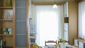 A compact kitchen with wooden cabinets, a dining table set with plates, bowls, and a fruit bowl. - Sea Daffodil Apartments (Kissamos)