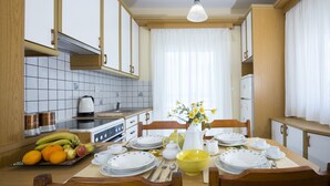 A clean, well-lit kitchen with white cabinets, a tiled backsplash, and a dining table set for four. - Sea Daffodil Apartments (Kissamos)