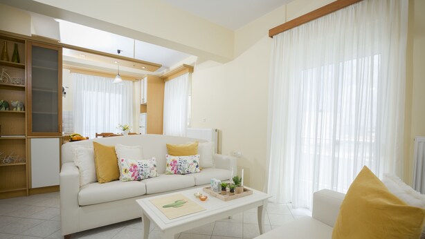 A spacious living room with a white sofa, a coffee table, and a dining area. - Sea Daffodil Apartments (Kissamos)