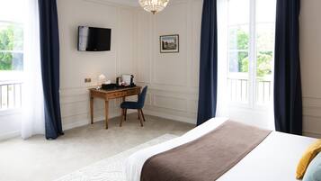 A bedroom with a bed, a desk, a chair, a television, and a chandelier.