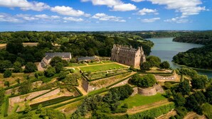 A historic castle with a large courtyard, surrounded by lush greenery and a river.