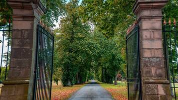 A pathway flanked by stone pillars and metal gates, leading through a park with trees and fallen leaves.