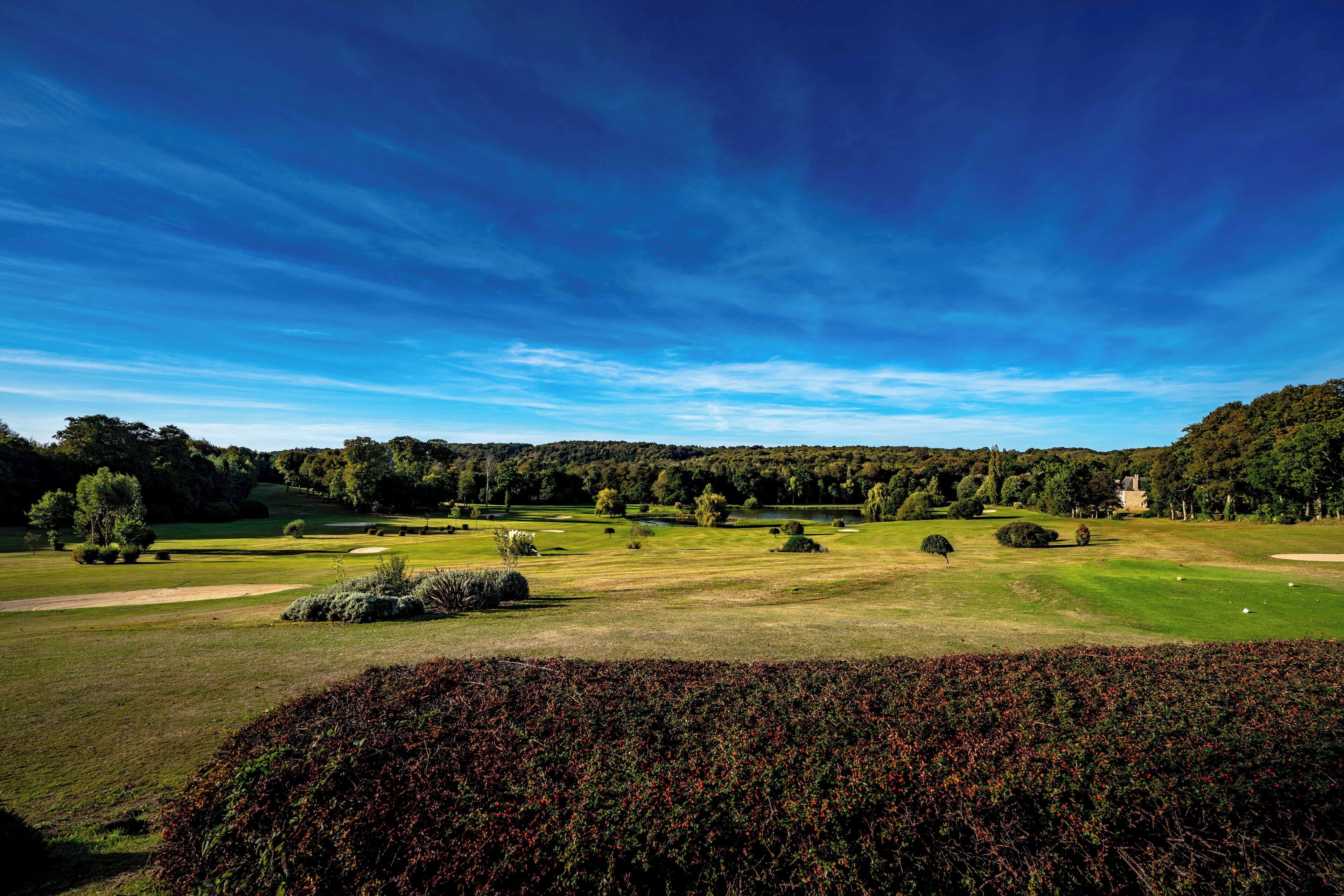Un parcours de golf avec un ciel dégagé, une pelouse bien entretenue et des arbres.