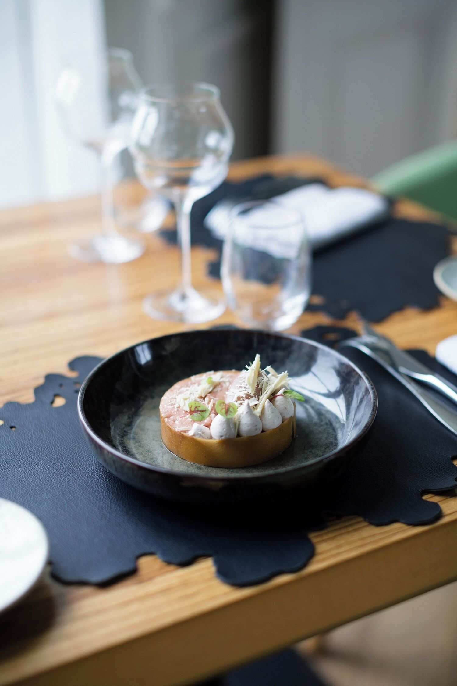 A dessert on a black plate with a scalloped edge, placed on a wooden table with a black placemat.