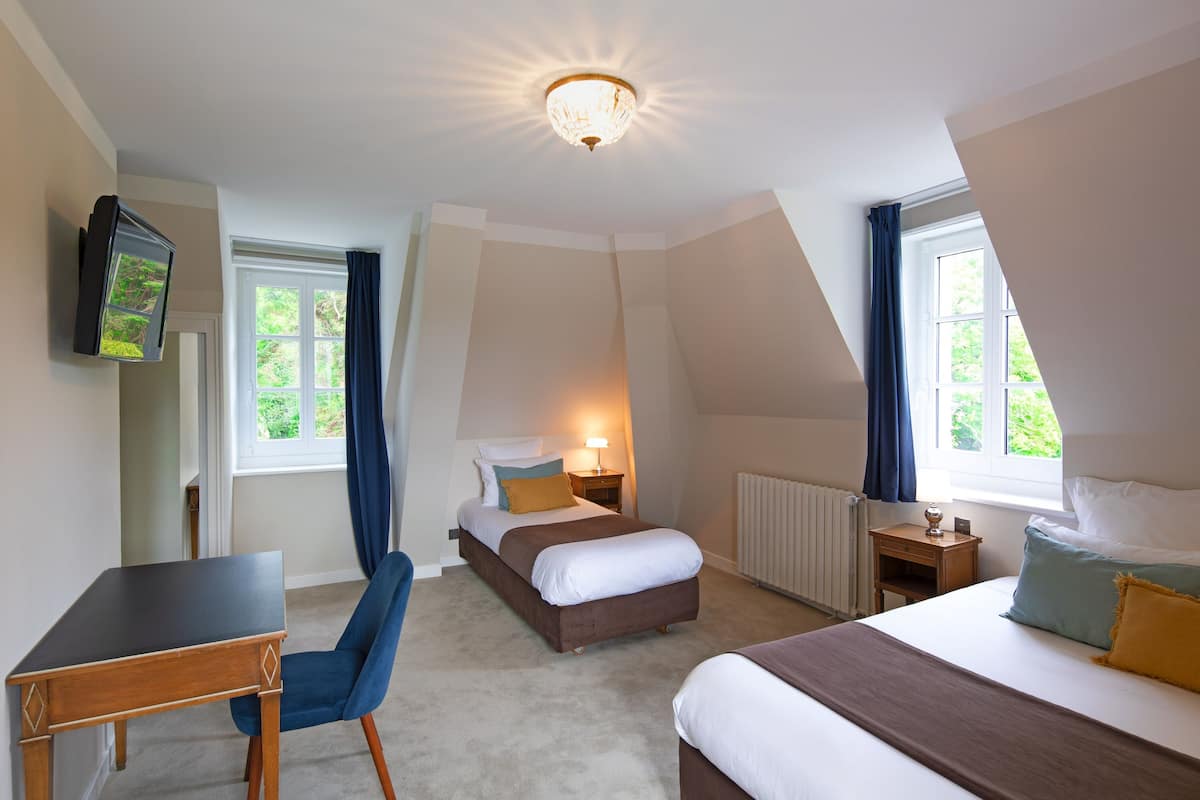 Une chambre avec un bureau, deux lits, une télévision et un luminaire au plafond.