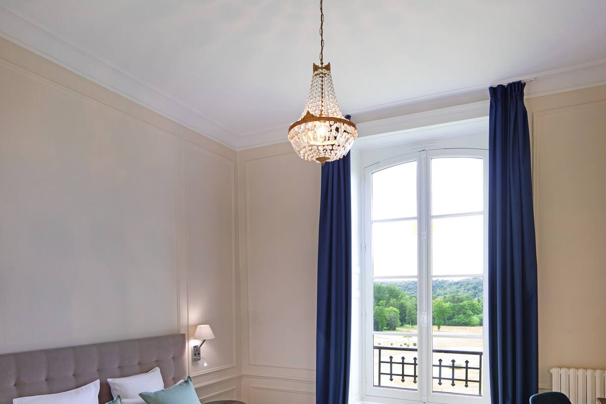 Une chambre d’hôtel avec un grand lit, un lustre, une vue sur l’extérieur et un fauteuil.