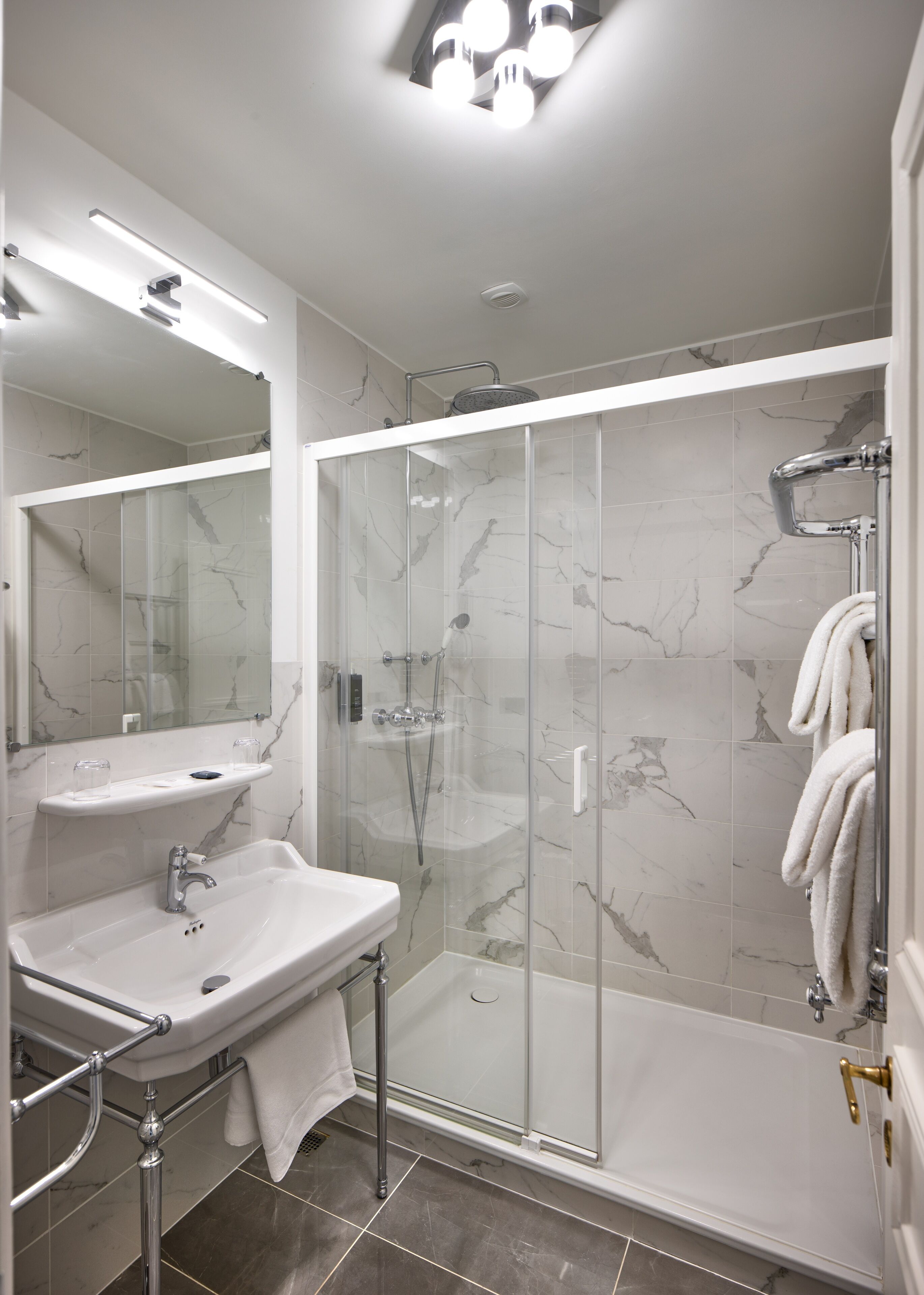 Een moderne badkamer met een douchecabine van glas, een witte wastafel met een marmeren aanrechtblad en een grote spiegel.