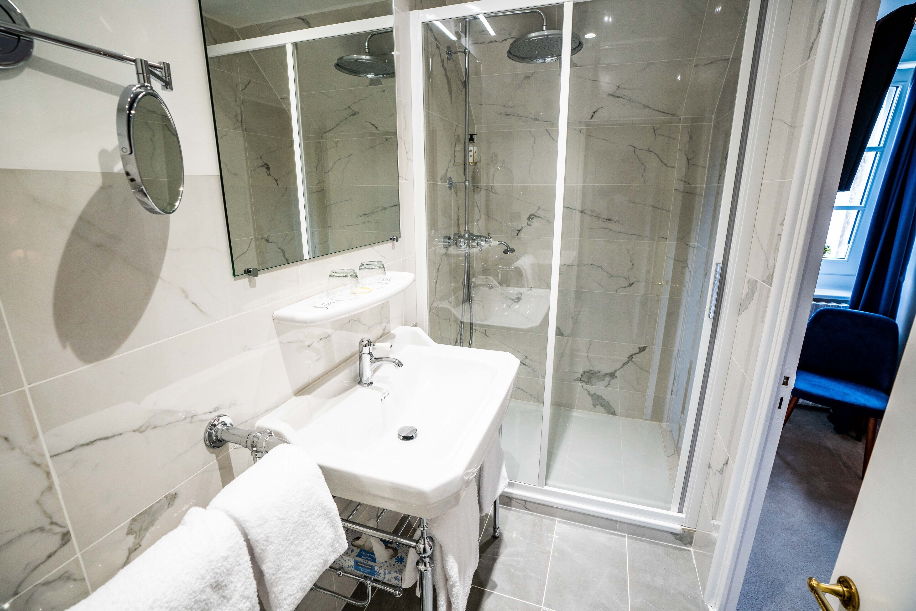Une salle de bain moderne avec un mur recouvert de carreaux de marbre, un lavabo blanc, un miroir et une douche à parois de verre.