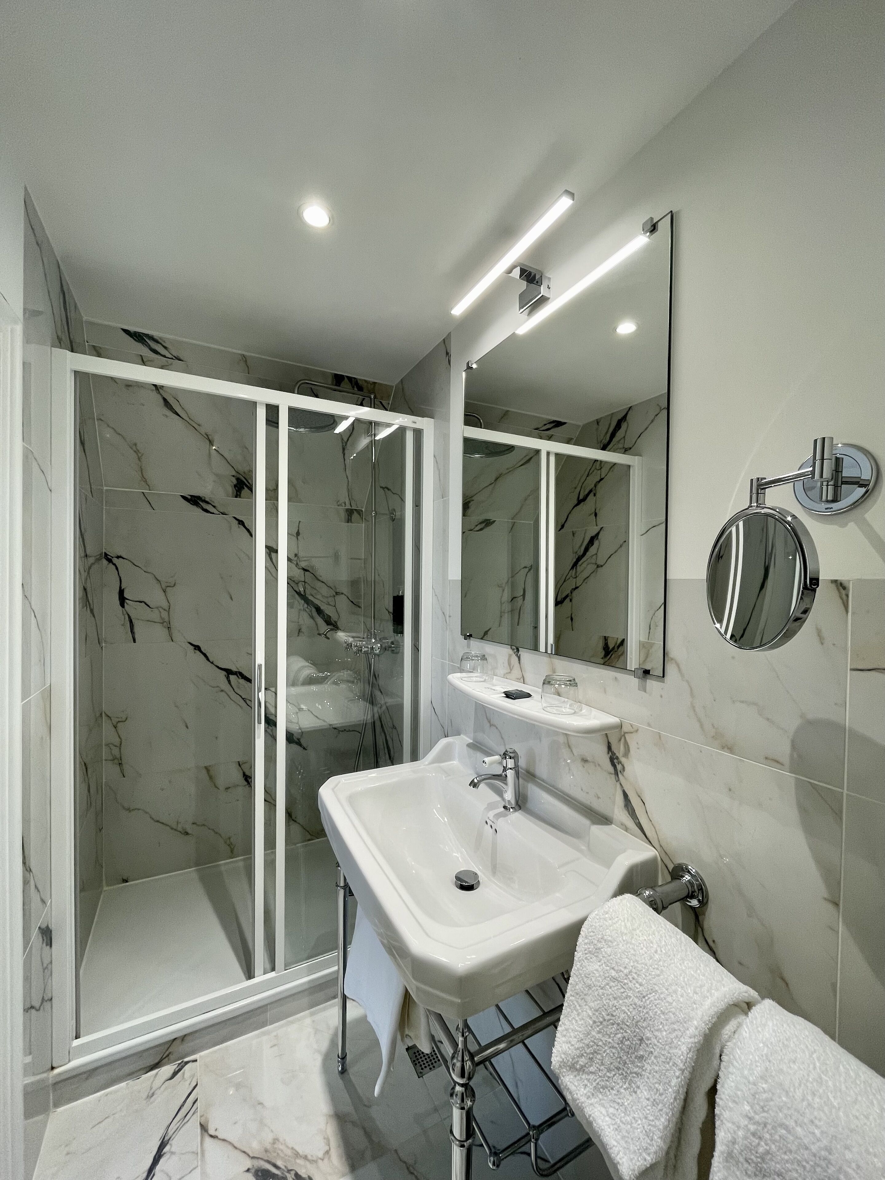 A modern bathroom with a glass shower enclosure, a white sink, and a large mirror.