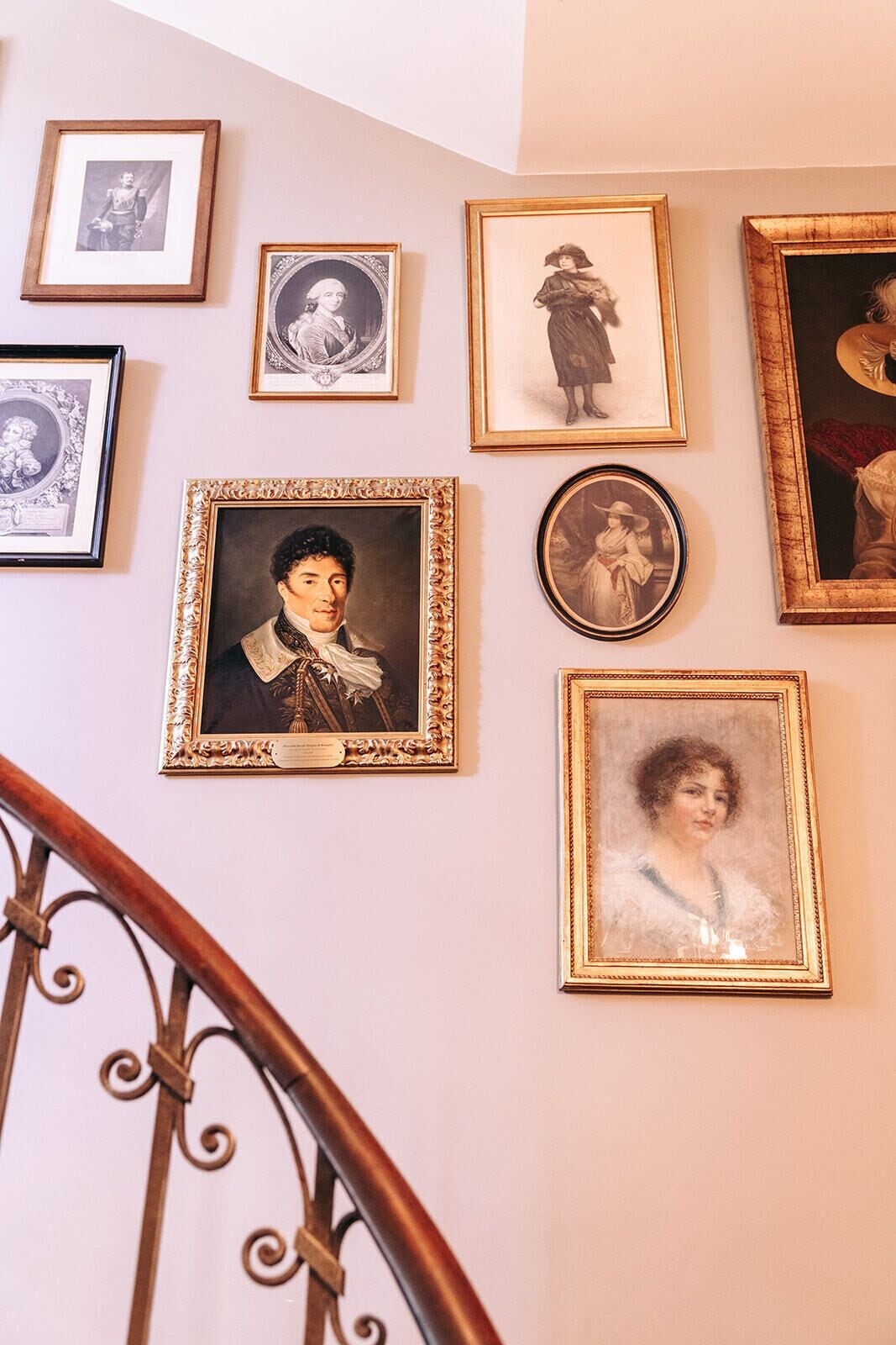 A staircase with ornate metal railings and a wall adorned with framed portraits.