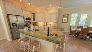 A modern kitchen with a central island, stainless steel appliances, and a dining area with wicker furniture.
