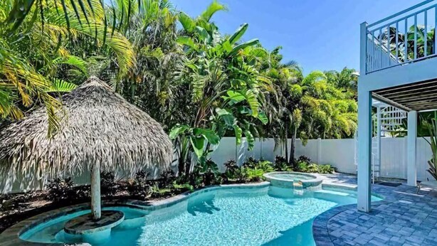 A swimming pool with a thatched roof structure, surrounded by lush tropical vegetation.