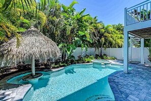 Una piscina con una estructura de techo de paja, rodeada de exuberante vegetación tropical.