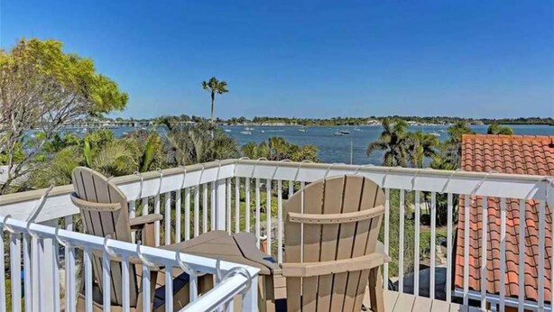 Un balcon avec deux fauteuils Adirondack et une table, donnant sur une marina où l’on peut admirer des bateaux et des palmiers.