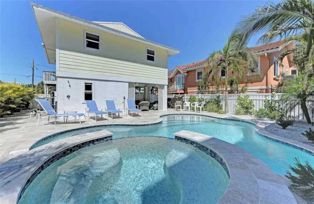 A two-story house with a swimming pool, surrounded by palm trees and other houses.