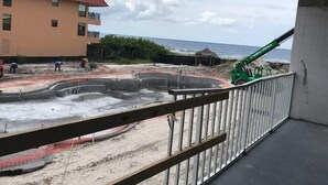 A construction site with workers, a green excavator, and a building in the background. - Deluxe King Gulf View Rm 209 Apartment 1 (Holmes Beach)