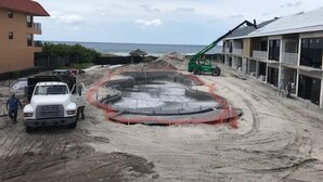 A construction site with a circular concrete structure, a white truck, and a green crane. - Deluxe King Gulf View Rm 212 Apartment 1 (Holmes Beach)
