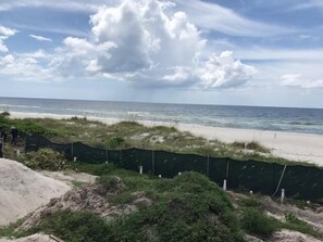 A beach view with a sandy shore, a fence, and a cloudy sky.