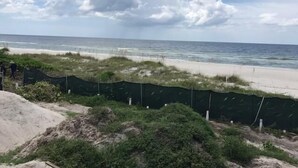 A beach view with a sandy shore, a fence, and a cloudy sky.