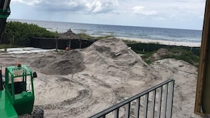 A view of a beach with sand piles and a thatched-roof structure. - Gulf View Suite 205 Apartment 1 (Holmes Beach)