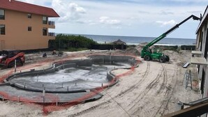 A construction site with a circular concrete structure, a green crane, and a building with a red roof. - Gulf View Suite 210 Apartment 1 (Holmes Beach)