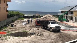 Un chantier de construction avec un camion blanc, une grue verte et des ouvriers.