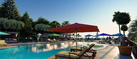 A pool area with lounge chairs and umbrellas, surrounded by palm trees and a clear sky.