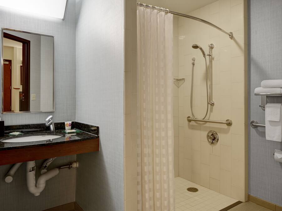 Un baño con lavamanos, espejo, ducha y toallero.