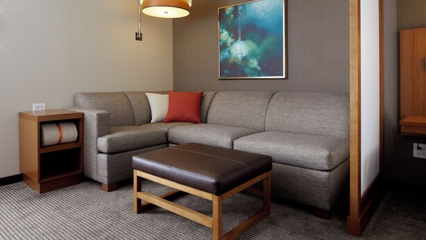 A modern living room with a sectional sofa, a wooden coffee table, a side table, and a wall-mounted lamp. - Hyatt Place Calgary Airport (Calgary)