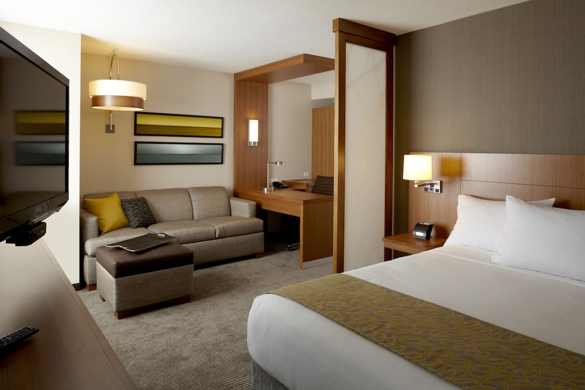 A hotel room with a bed, a sofa, a desk, a TV, and a lamp.