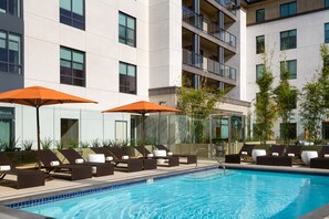 A pool area with lounge chairs and umbrellas, surrounded by a modern building with multiple floors and balconies. - Hyatt Place Pasadena (Pasadena)
