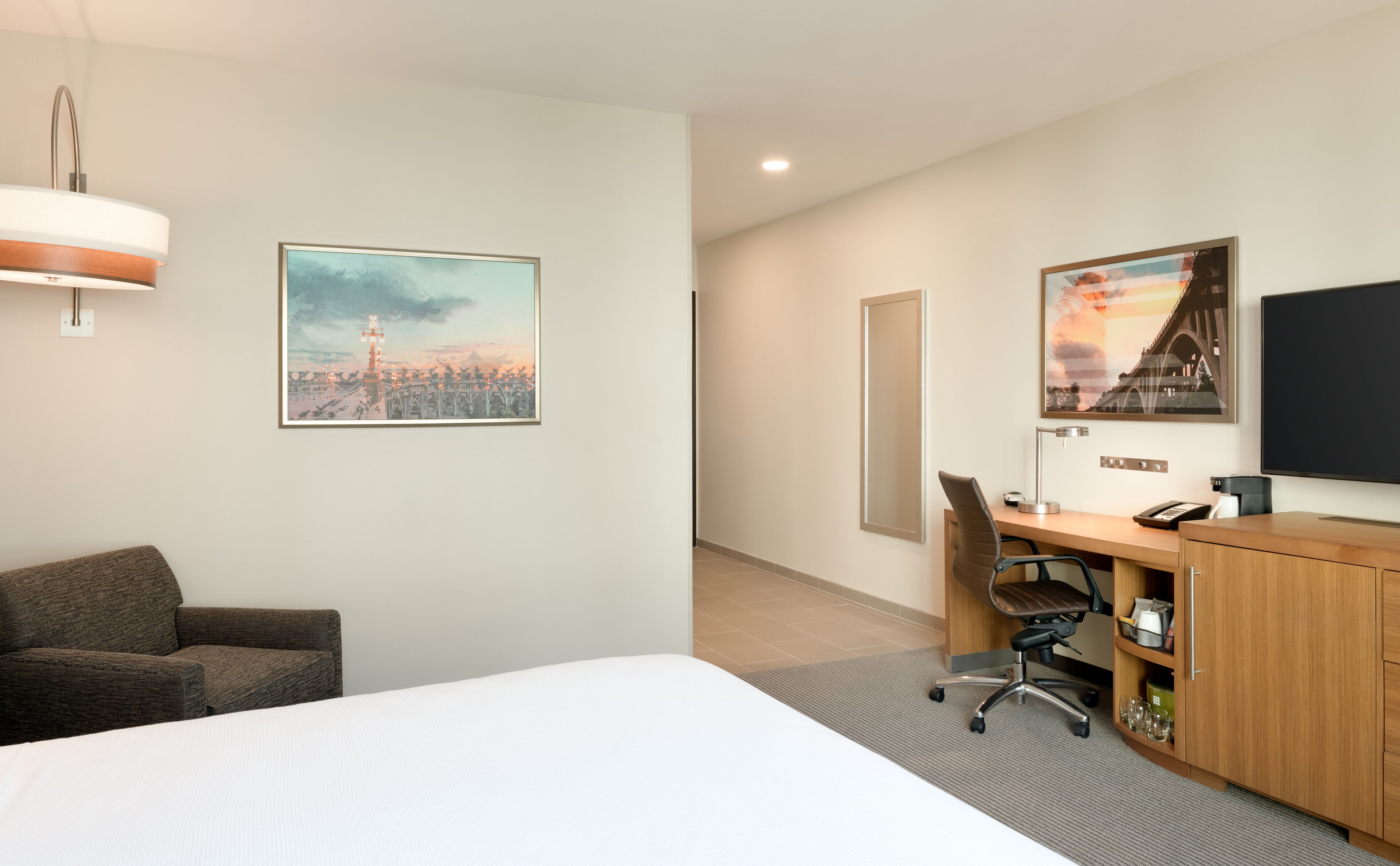 Habitación de hotel con cama, escritorio con silla, televisión y obras de arte en las paredes.
