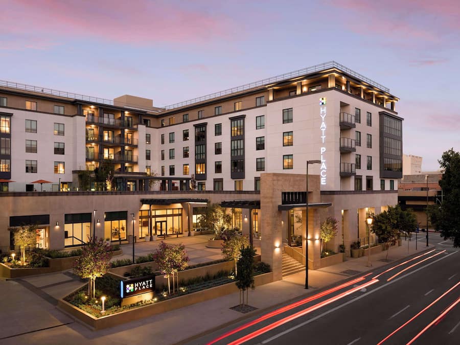 A multi-story hotel with a modern design, featuring balconies, large windows, and a well-lit entrance area.
