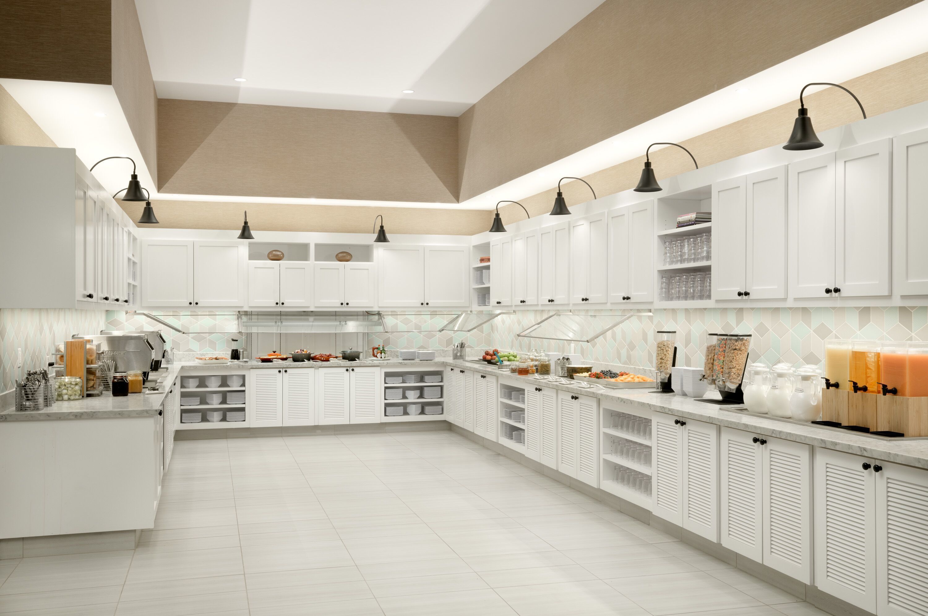 A modern kitchen with white cabinets, black pendant lights, and a tiled floor.