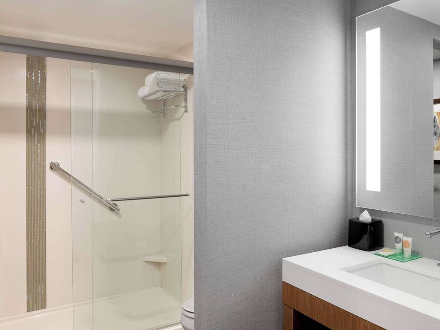 A modern bathroom with a glass shower enclosure, a white sink with a mirror, and a towel rack.