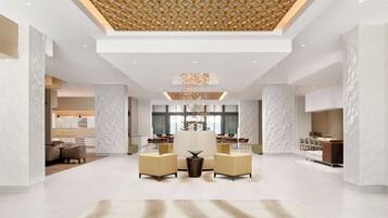 A spacious lobby with a modern design, featuring a central seating area with sofas and a decorative plant.