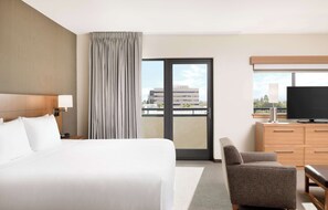 A hotel room with a large bed, a chair, a TV, and a view of a building through the window. - Hyatt Place Pasadena (Pasadena)