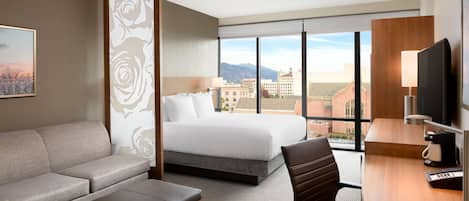 A hotel room with a bed, a sofa, a desk, and a TV.