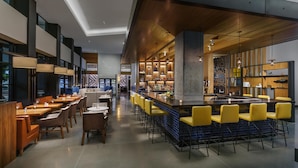 Un espace bar moderne doté d’un long comptoir, de tabourets de bar jaunes et de différents types de sièges, notamment des tables et des chaises.