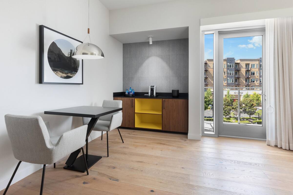 A modern kitchen with a dining area, a large window, and a view of buildings.