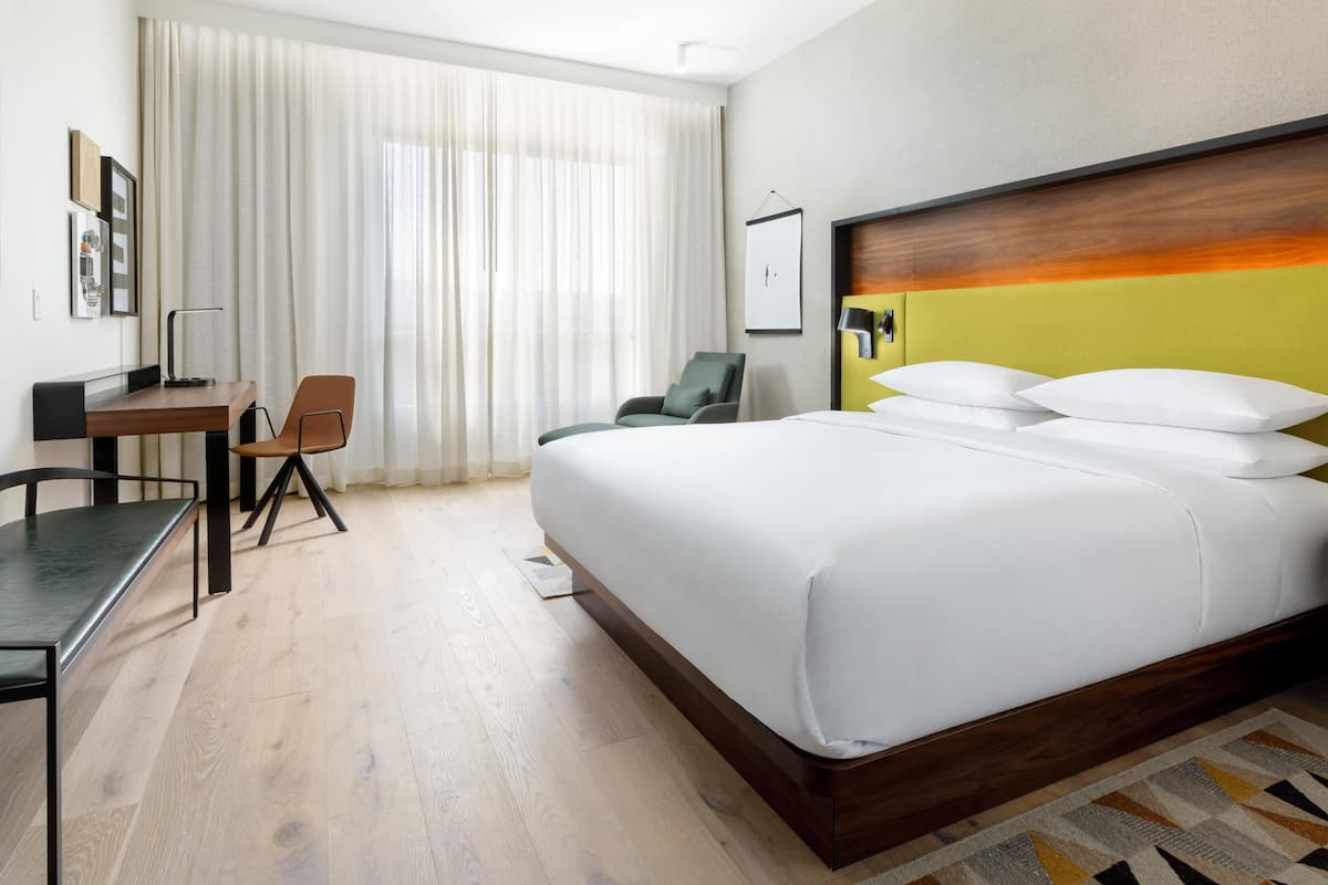 A hotel room with a bed, a desk, a chair, and a large window with curtains.