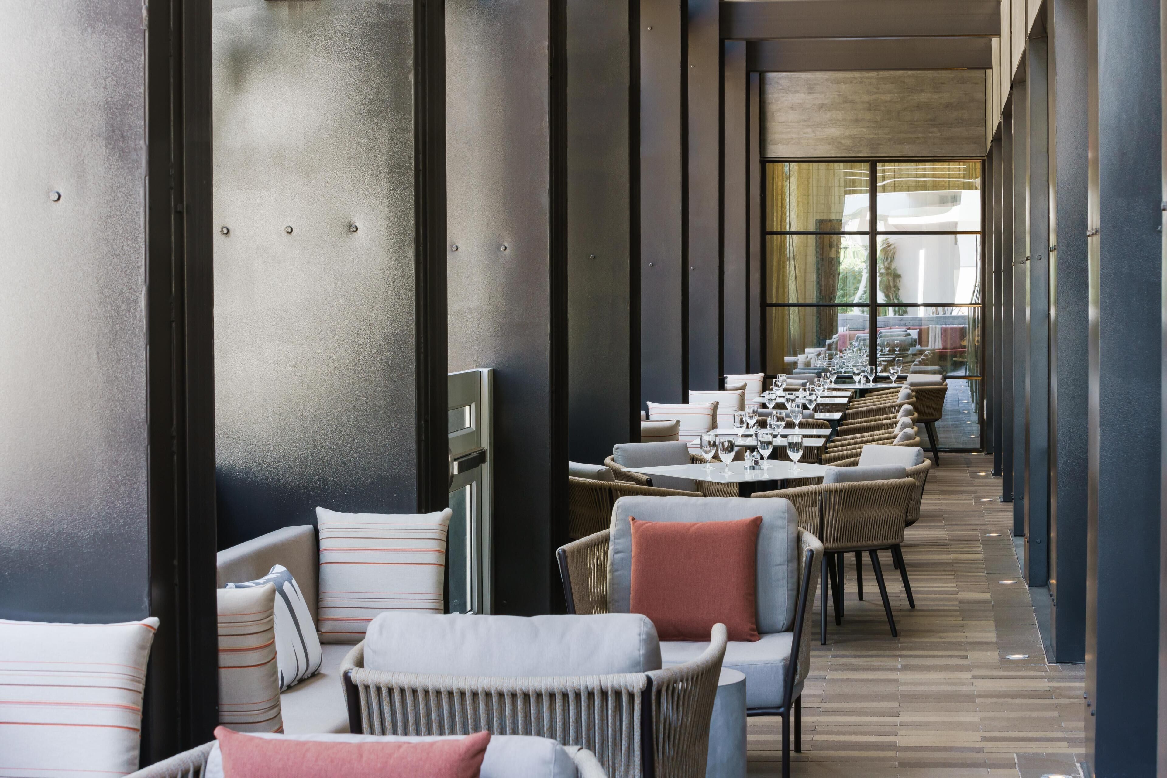 A modern indoor dining area with long tables, chairs, and a view through large windows.