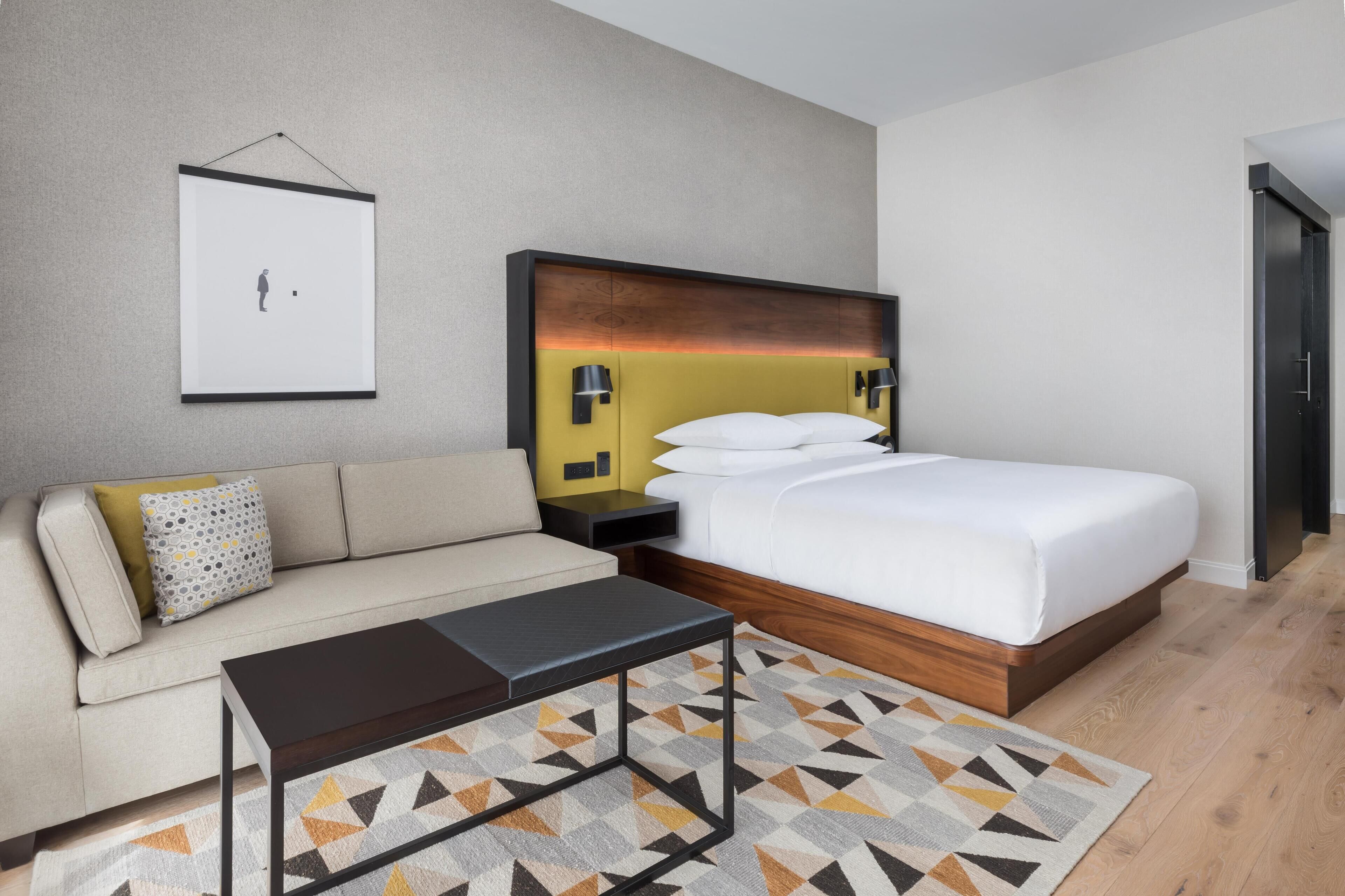Habitación de hotel con cama, sofá, una mesita de café, un cuadro en la pared y una puerta.