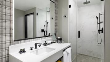 A modern bathroom with a large mirror, a white sink, a shower with a handheld showerhead, and a towel rack.