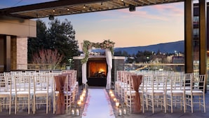 Un lieu de cérémonie de mariage en plein air, avec une allée blanche, des chaises de chaque côté et une cheminée au bout.
