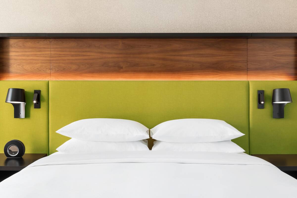 A bed with white linens, a green headboard, and two wall-mounted lamps.