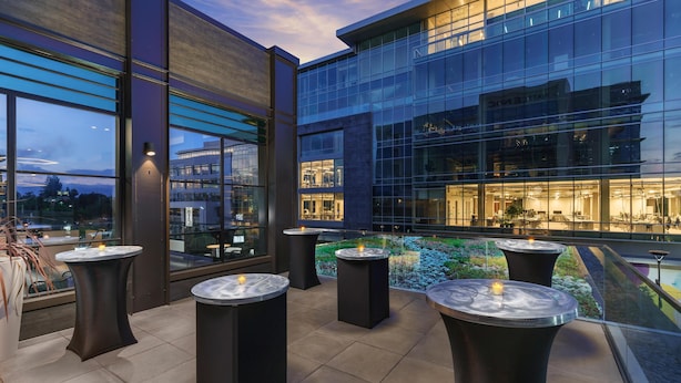 Un bâtiment moderne avec une façade dotée de grandes fenêtres et une terrasse sur le toit, aménagée avec des tables rondes et des bougies.