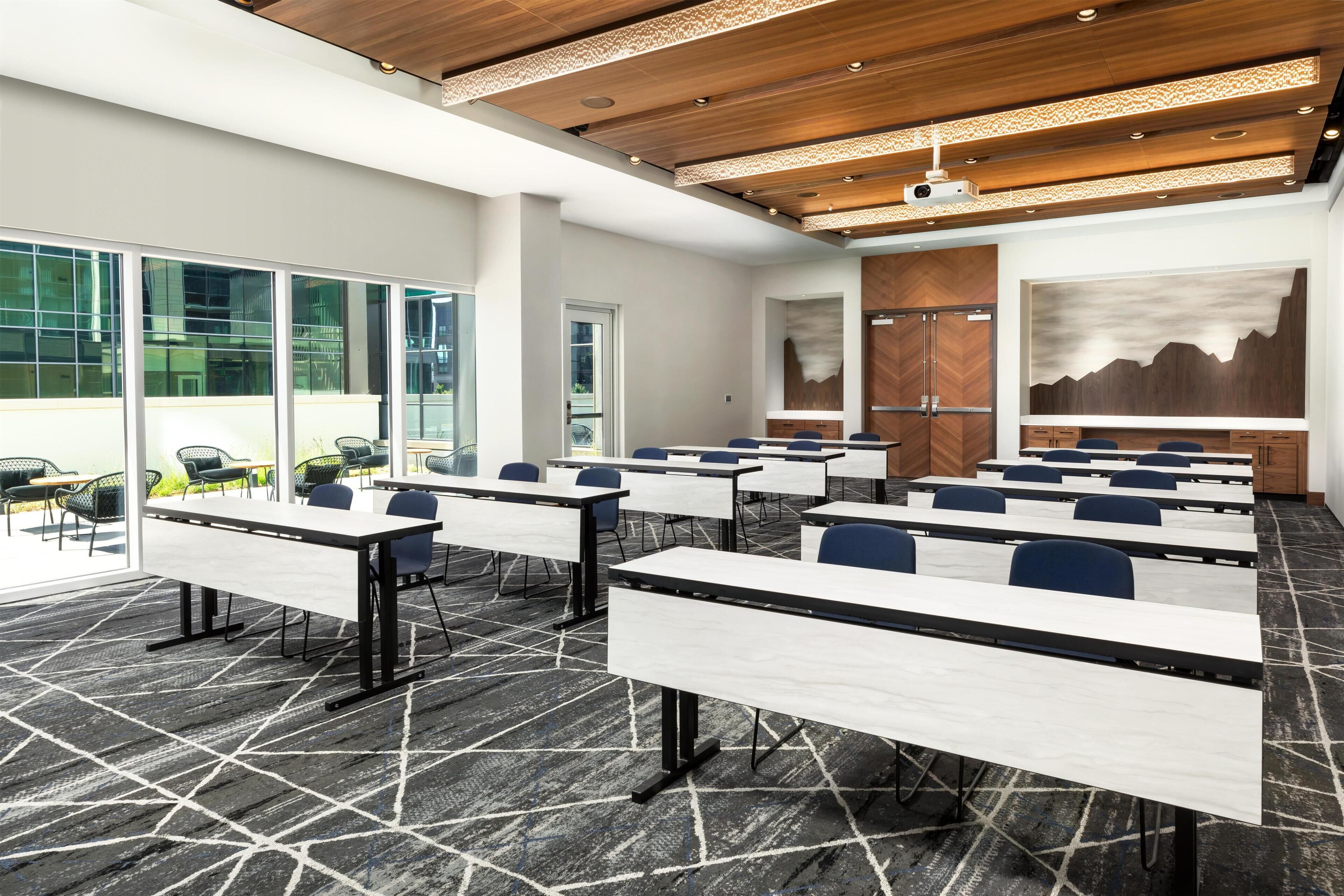 A conference room with tables, chairs, a projector, and a large window.