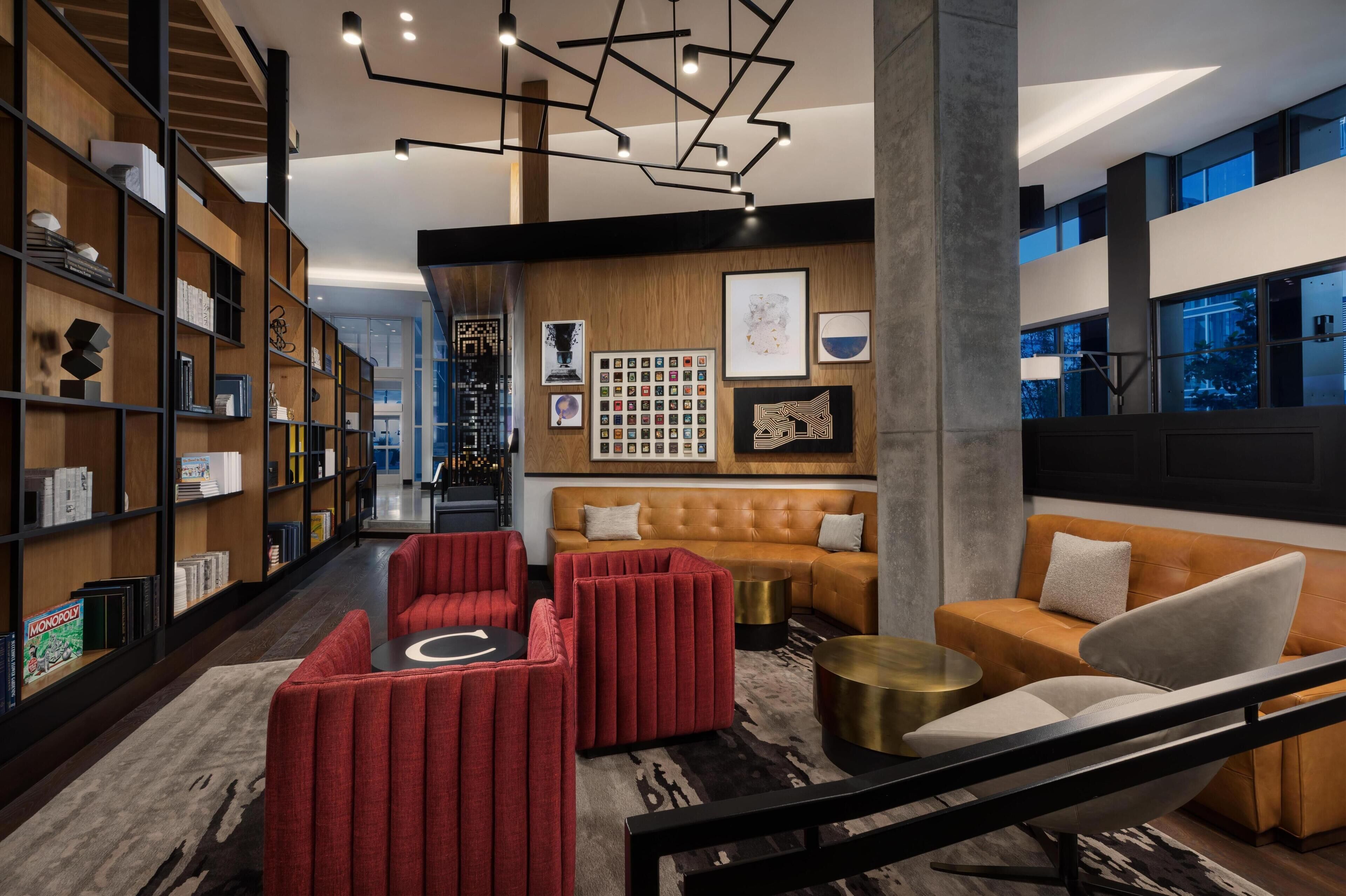 A modern interior with a leather sofa, red upholstered chairs, a bookshelf, and a wall with framed pictures.