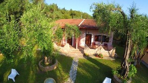 A house with a red-tiled roof, surrounded by lush greenery and stone pathways. - Anneta Studios (Igoumenitsa)